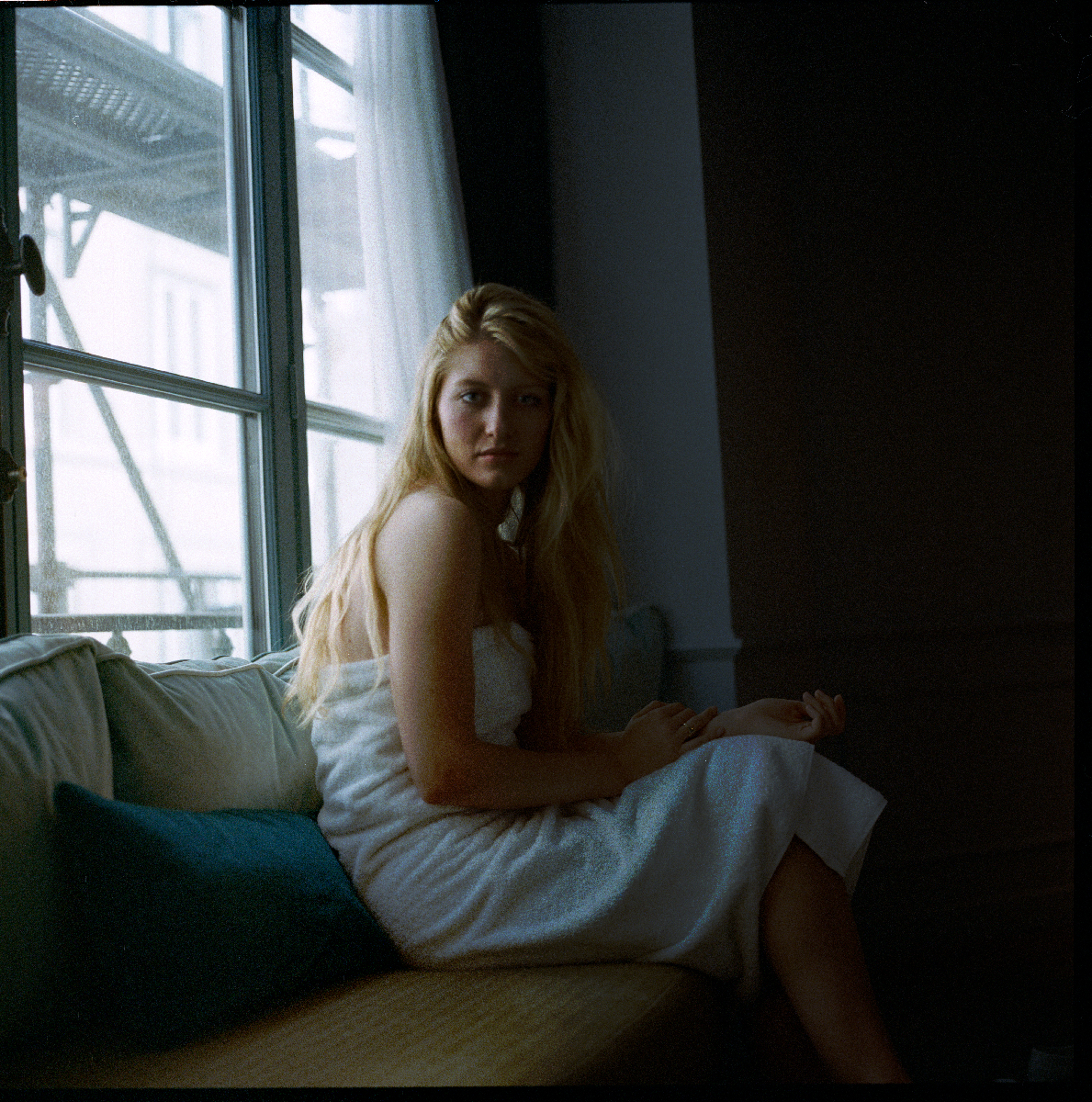 Jeune femme blonde assise sur un canapé près d'une fenêtre, lumière naturelle douce