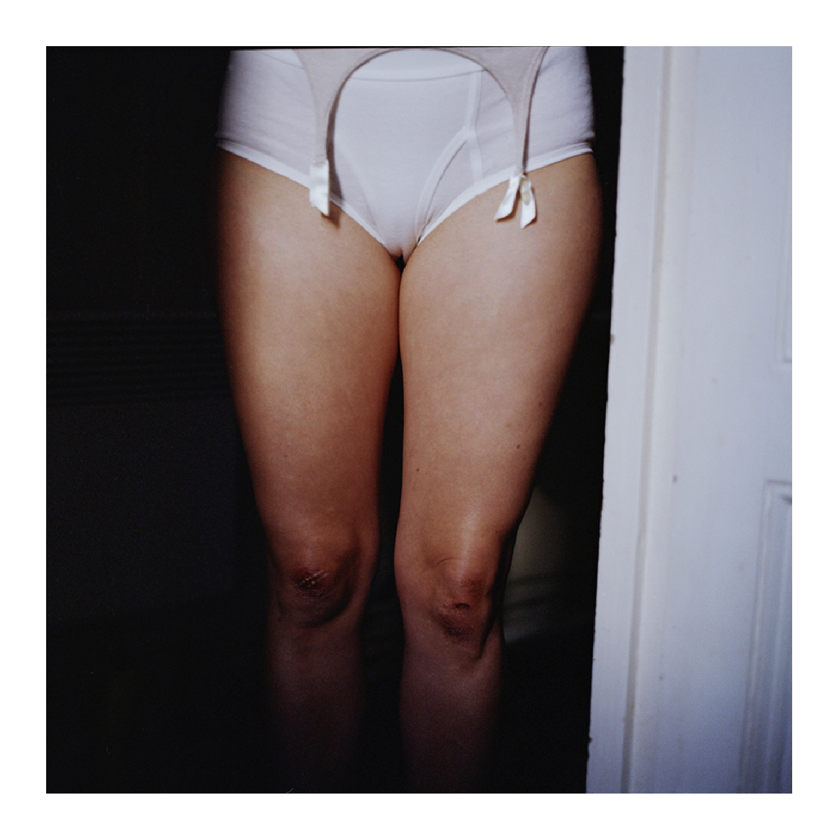 Cadrage serré sur les jambes et la lingerie blanche d'une femme dans l'embrasure d'une porte